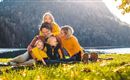 A family is sitting on a meadow by the shore of a lake. They are wearing cheerful yellow clothing and enjoying a sunny day in nature.