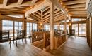 A cozy interior with a wooden ceiling and large windows. The room is furnished with comfortable chairs and natural light.