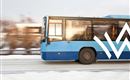 Ein blauer Bus fährt schnell auf einer schneebedeckten Straße. Im Hintergrund sind unscharfe Bäume sichtbar.