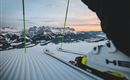 Eine Skisicht auf schneebedeckte Berge im Hintergrund. Im Vordergrund sind Skier und ein Skischuh zu sehen.