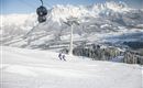 A beautiful winter landscape with snow-covered mountains. Skiers enjoy the descent under a cable car.