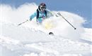 A skier glides through fresh snow in the mountains. The sky is clear and blue, perfect for a fantastic ski day.