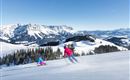 A beautiful winter sports area with snow-covered slopes and mountains in the background. Two skiers enjoy the sun and the fresh air.