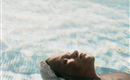 A man is lying relaxed on the water in a pool. The gentle waves reflect the light and create a calm atmosphere.