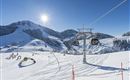 An idyllic winter landscape with skiing slopes and a chairlift. The sky is clear and the sun is shining over the snow-covered mountains.