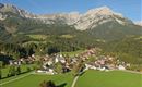 A picturesque mountain landscape with a small town in the valley. The surroundings are green and surrounded by majestic mountains.