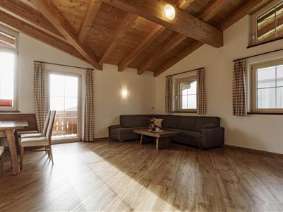 A cozy living room with a wooden ceiling and large windows. There is a sofa, a table, and stylish decorative elements.