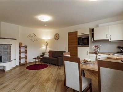 A modern living room with a cozy couch and dining table. The wooden floors and the kitchenette give the room a warm atmosphere.
