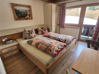 Ein gemütliches Zimmer mit zwei Einzelbetten und einem Holzlook. Große Fenster bieten viel Tageslicht und einen Blick auf den Balkon.