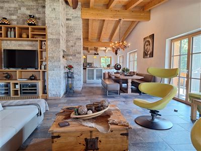 Een moderne woon- en eetkamer met houten balkenplafond en grote ramen. De inrichting omvat een gezellige bank, een eethoek en stijlvolle decoratieve elementen.