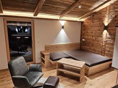 Pohodlná místnost s dřevěným obložením a teplým světlem. Křeslo a malý stůl jsou umístěny v rohu.