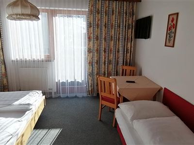 A cozy hotel room with two single beds and a table. Large windows provide plenty of daylight and a view outside.