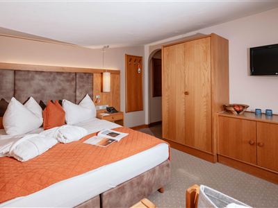 Ein gemütliches Hotelzimmer mit einem großen Bett und rustikalen Holzmöbeln. Der Raum ist hell und einladend, mit modernem Komfort.
