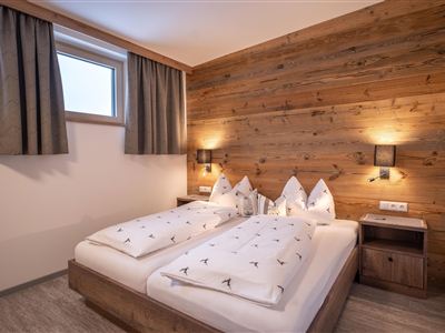 Een gezellige slaapkamer met twee bedden en houtelementen. Grote ramen laten veel daglicht binnen.