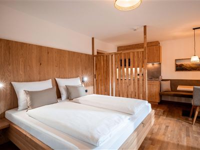 Světlý, moderní obytný/spací prostor s manželskou postelí, teplým dřevěným nábytkem a útulným posezením.