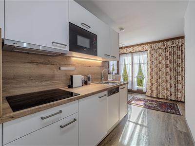 Eine moderne Küche mit weißen Schränken und Holzakzenten. Im Hintergrund sind Vorhänge und ein Teppich sichtbar.