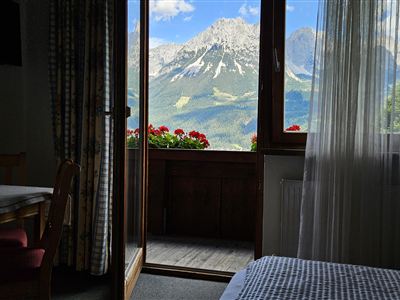 A cozy room with a view of the mountains. The balcony doors open to a beautiful panorama with blooming plants.