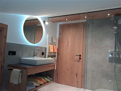 Ein modernes Badezimmer mit einer Holzstruktur und schlichten Fliesen. Der Waschplatz hat ein rundes Licht und ist mit bunten Handtüchern dekoriert.