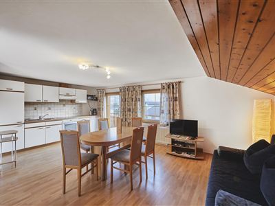A bright and spacious living kitchen with a wooden ceiling. The room is equipped with a dining table, chairs, and a cozy sofa.