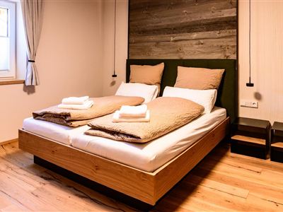 A cozy bedroom with a large double bed and soft bedding. The natural wood and green tones create a relaxed atmosphere.