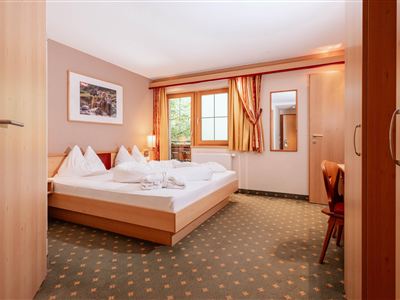 Ein gemütliches Zimmer mit einem Doppelbett und hellen Textilien. Der Raum hat ein Fenster mit Blick nach draußen und ist harmonisch eingerichtet.