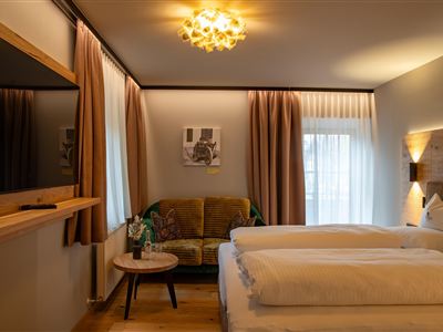 A modern bedroom with two beds and a cozy sofa. The decor is stylish and bright, with large windows that let in plenty of light.