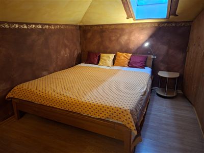 A cozy bedroom with a large bed and colorful pillows. The room has a warm color scheme and a window in the roof.