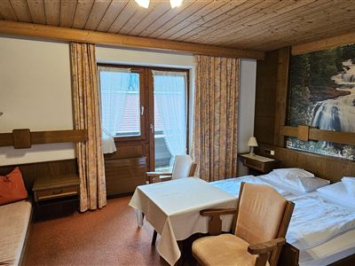 Een gezellig hotelkamer met een tweepersoonsbed en een bank. De wand is versierd met een mooi natuurmotief, en er is een balkon met toegang naar buiten.