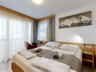 A modern bedroom with a double bed and large windows. The room has wooden details and offers a cozy atmosphere.