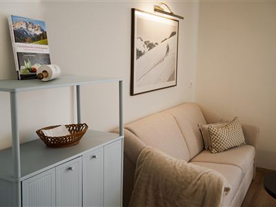 Een gezellige woonkamer met een lichte bank en een kleine tafel. Aan de muur hangt een afbeelding van een berglandschap.