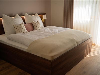 Een knusse slaapkamer met een groot bed en zachte kussens. Zacht licht valt door de gordijnen en creëert een uitnodigende sfeer.