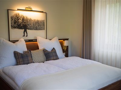 Een gezellige slaapkamer met een groot bed en zachte kussens. Aan de muur hangt een schilderij van een winterbos.