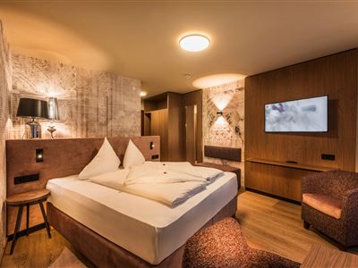 Ein modernes Hotelzimmer mit einem Doppelbett, einem Flachbildfernseher und stilvollen Holzmöbeln. Die Wände sind mit einem eleganten Muster dekoriert, und der Raum wirkt gemütlich und einladend.