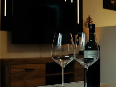 An elegant table with two wine glasses and a bottle of wine. In the background, there is a modern television and stylish wall lights.