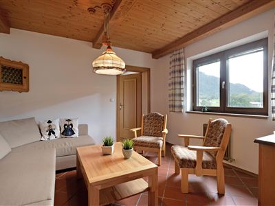 Ein gemütlicher Wohnraum mit einem hellen Sofa und zwei Holzstühlen. Große Fenster sorgen für viel Licht und bieten einen Blick auf die umliegende Landschaft.