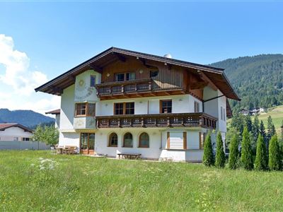 A beautiful, traditional house in the mountains with a green lawn and a view of the surrounding forests. The sky is clear and sunny.