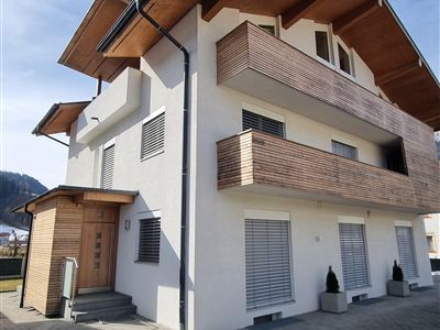 Een modern huis met houten bekleding en grote balkons. De heldere lucht en de geplaveide oprit geven het gebouw een uitnodigende uitstraling.