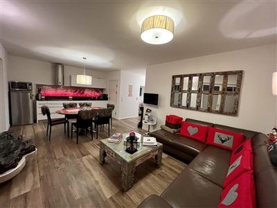 Eine moderne Wohnküche mit einem großen Sofa und einem Essbereich. Die Wände sind hell, und die Dekoration ist stilvoll mit roten Akzenten.