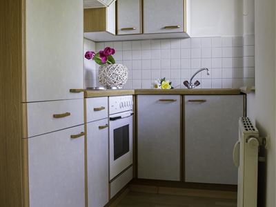 Een moderne keuken met lichte kasten en een houten plafond. Op het aanrecht staan bloemen en verschillende keukengerei.