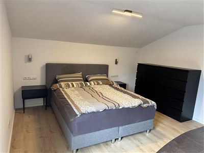 Ein modernes Schlafzimmer mit einem großen Bett und einer schlichten Kommode. Die Wände sind hell und der Boden ist aus Holz.