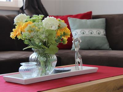 A beautifully arranged flower bouquet in a glass vase sits on a table. Next to it are two glasses and a decorative figure.