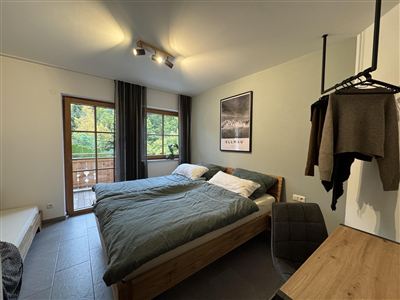 Ein gemütliches Schlafzimmer mit zwei Einzelbetten und Fensterblick auf die Natur. Die Einrichtung ist modern und einladend, mit einem Holzschreibtisch und einem Wandregal.