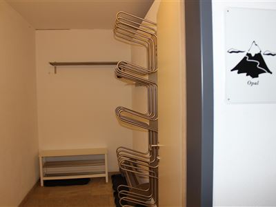 Een eenvoudige kleedruimte met een lichte, neutrale uitstraling. Aan de linkerkant zijn er stangen voor kleding en een bank.