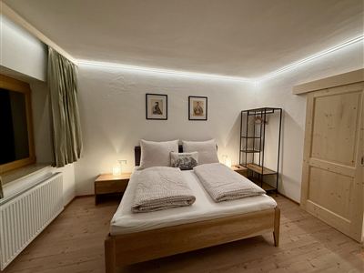 Ein gemütliches Schlafzimmer mit einem großen Bett und hellen Wänden. Der Raum ist stilvoll mit einem Bücherregal und Bildern dekoriert.