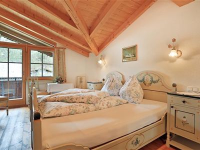 Een gezellige slaapkamer met houten plafond en twee sets beddengoed. De kamer heeft grote ramen die veel licht binnenlaten en een rustieke inrichting.