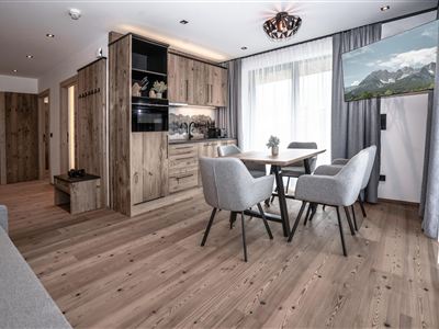 Een modern ingerichte ruimte met een open keuken en een eetgedeelte. Grote ramen laten veel licht binnen en bieden uitzicht op de bergen.