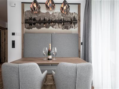 Een elegante eetruimte met een houten tafel en twee grijze stoelen. Op de tafel staan een fles champagne en twee glazen, omringd door moderne decoratieve verlichting.