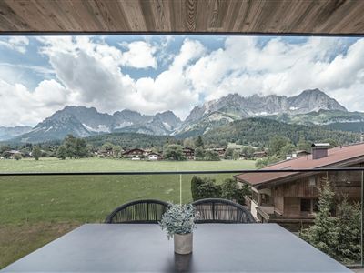 Een adembenemend uitzicht op de bergen met wolken en weelderige weilanden. Op de voorgrond staat een tafel met een kleine plant.