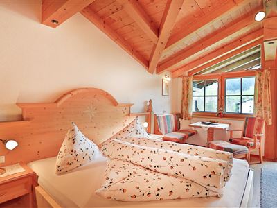 Een gezellige kamer met houten wandbekleding en grote ramen. Er is een groot bed en een zithoek met mooie decoratie.