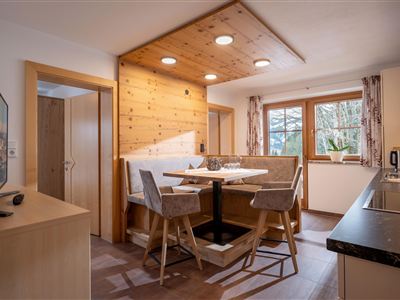 Een gezellige keuken met een eetgedeelte en houten panelen. Grote ramen zorgen voor veel licht en een uitzicht naar buiten.